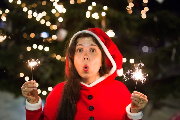 Urlaub, Glück, Menschen - junge Frau im Weihnachtsanzug lächelt mit Lichtern in der Hand am Weihnachtsbaum — Stockfoto