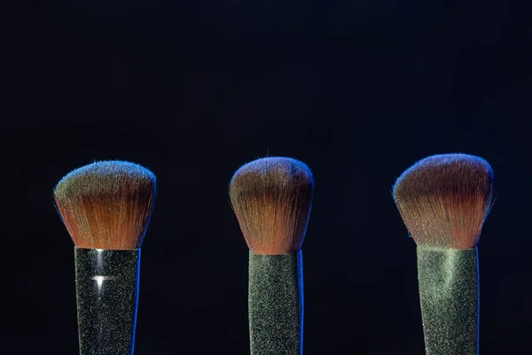 Maquillaje mineral y concepto de objetos - Tres pinceles de maquillaje con polvo azul sobre fondo oscuro —  Fotos de Stock