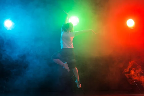 Animadora joven bailando sobre fondo oscuro colorido — Foto de Stock