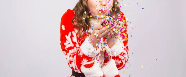 Красивая девушка в костюме Санты приветствует новый 2019 год, раздувая конфетти перед камерой. Новогодние праздники и вечеринки — стоковое фото