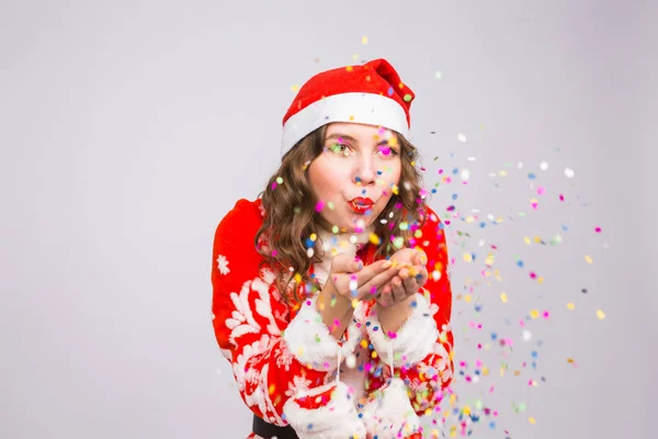 La gente, la Navidad y el concepto de vacaciones - bastante joven dama en traje de Santa Claus soplando confeti sobre fondo blanco — Foto de Stock