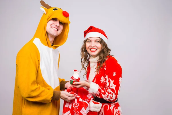 Noël, célébration, concept de personnes - Homme drôle en costume de cerf et femme en costume de Père Noël tenant une figurine de Père Noël dans les mains — Photo