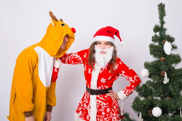 Vacances, Noël et concept de blague - Homme drôle en costume de cerf et femme en costume de Père Noël près de l'arbre de Noël sur fond blanc — Photo