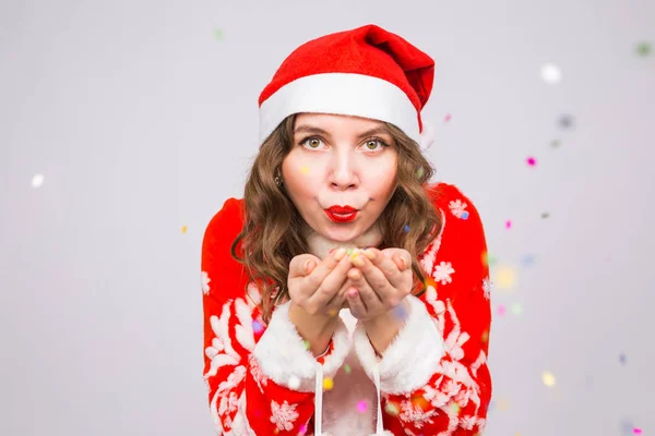 La gente, la Navidad y el concepto de vacaciones - bastante joven dama en traje de Santa Claus soplando confeti sobre fondo blanco — Foto de Stock