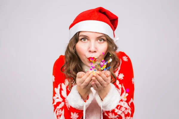 Menschen, Weihnachts- und Feiertagskonzept - hübsche junge Dame im Weihnachtsmann-Kostüm pustet Konfetti auf weißem Hintergrund — Stockfoto