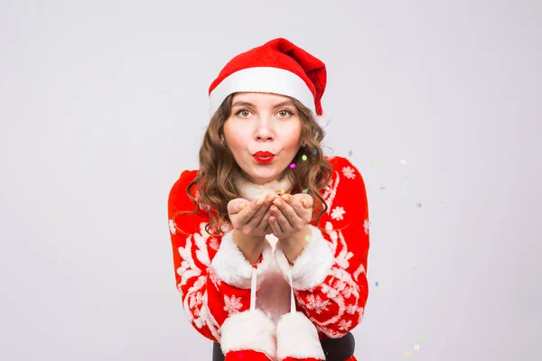 Menschen, Weihnachts- und Feiertagskonzept - hübsche junge Dame im Weihnachtsmann-Kostüm pustet Konfetti auf weißem Hintergrund — Stockfoto