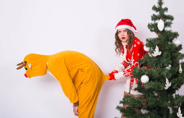 Noël, vacances et concept de blague - Femme drôle en costume de Père Noël et l'homme en costume de cerf folie autour près de l'arbre de Noël sur fond blanc — Photo