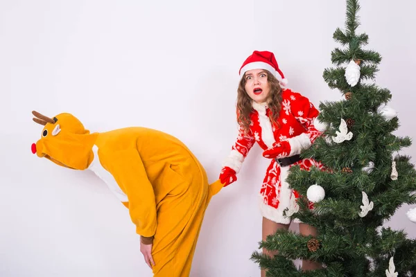 Divertimento, conceito de Natal e feriados mulher engraçada em terno de Papai Noel segurando a cauda do homem em traje de veado no fundo branco — Fotografia de Stock