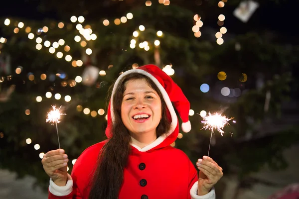 休日、幸福、人コンセプト - 彼女の手でライトとクリスマス ツリーの近く笑顔クリスマス スーツの若い女性 — ストック写真