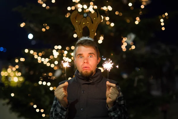 Gente, vacaciones y el concepto de Navidad - hombre sorprendido en cuernos de ciervos sosteniendo dos bengalas luz o bengalas al aire libre — Foto de Stock