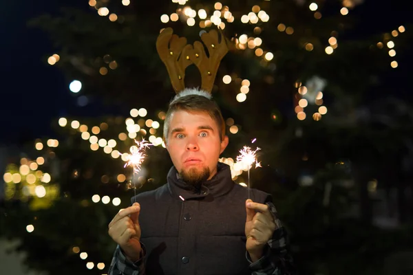 Mensen, vakantie en Kerstmis concept - grappige jongeman in Kerstmis herten kostuum met bengals licht buiten — Stockfoto