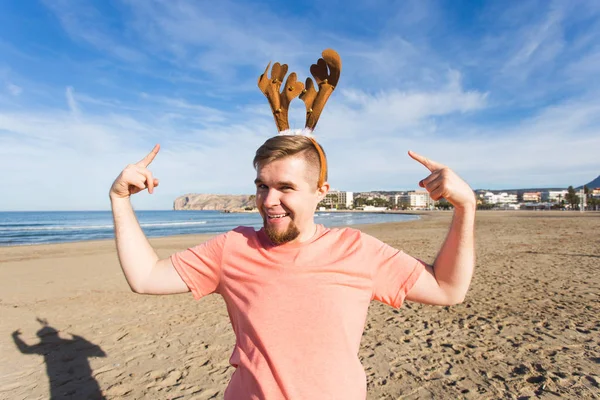Plezier, vakantie en reizen-concept - gelukkig man in Kerstmis herten hoorns op het strand — Stockfoto