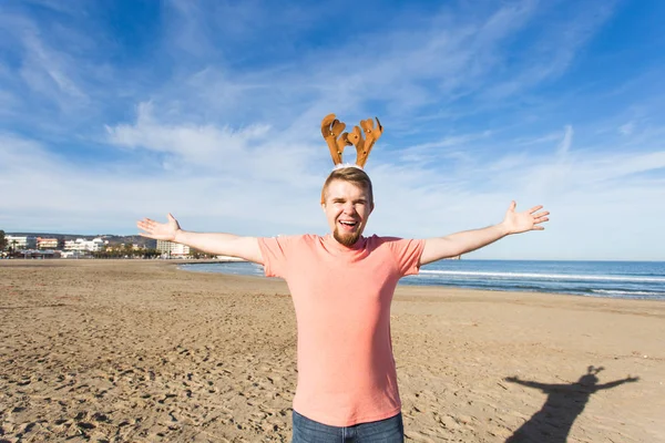 Plezier, vakantie en reizen-concept - gelukkig man in Kerstmis herten hoorns op het strand — Stockfoto