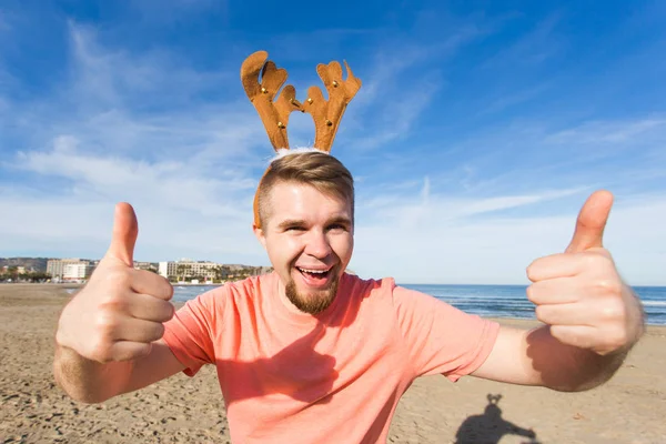 Feestdagen en Kerstmis concept - Man dragen herten hoorns met duimen omhoog op het strand — Stockfoto