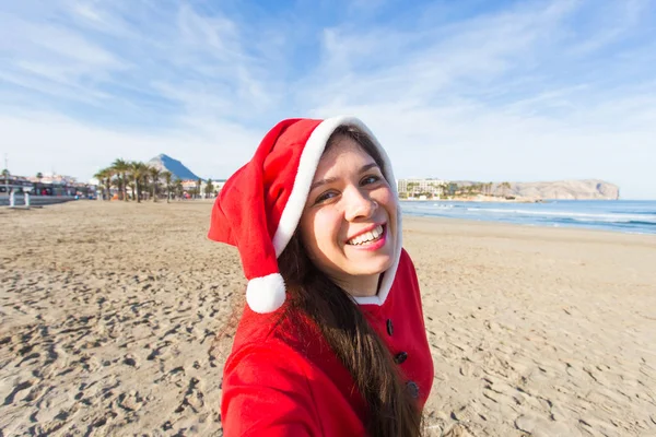Koncepcja ludzie, wakacje i święta - młoda kobieta w stroju santa biorąc selfie na plaży — Zdjęcie stockowe