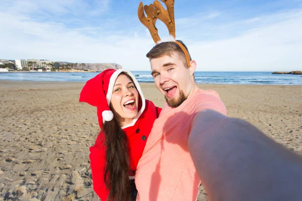 Zabawa i zimowe wakacje koncepcja - szczęśliwa para w Kostiumy sylwestrowe biorąc selfie na tle piaszczystej plaży — Zdjęcie stockowe