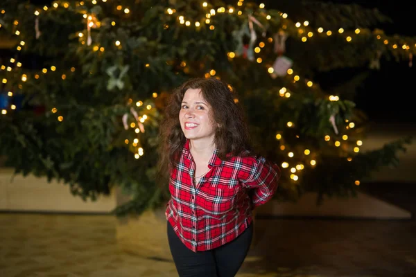 Holiday, Christmas and people concept - Young woman posing over Christmas tree background at night