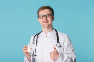 İlaç ve ilaç kavramı - erkek doktorunuza veya eczacınıza üzerinde mavi arka plan baş parmakları burun spreyi gidiyor