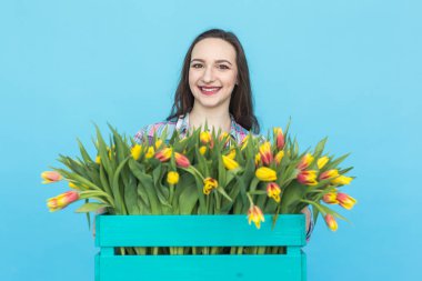 Gülüyor ve lale mavi arka plan üzerinde büyük kutu tutan mutlu beyaz kadın çiçekçi
