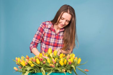 Güzel çiçekçi kadın mavi zemin üzerine sarı laleler ile. Floristics, tatil ve hediyeler kavramı