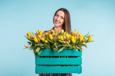 Gülüyor ve lale mavi arka plan üzerinde büyük kutu tutan mutlu beyaz kadın çiçekçi