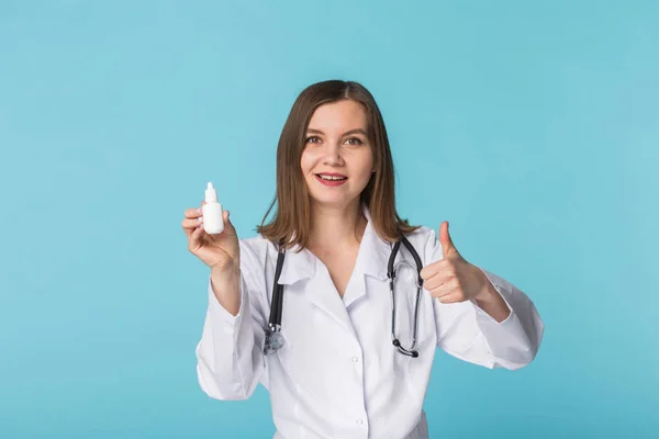 Produktami leczniczymi i farmaceutycznych koncepcja - młoda lekarka lub farmaceutą trzymając aerozol do nosa z kciuki do góry na niebieskim tle — Zdjęcie stockowe