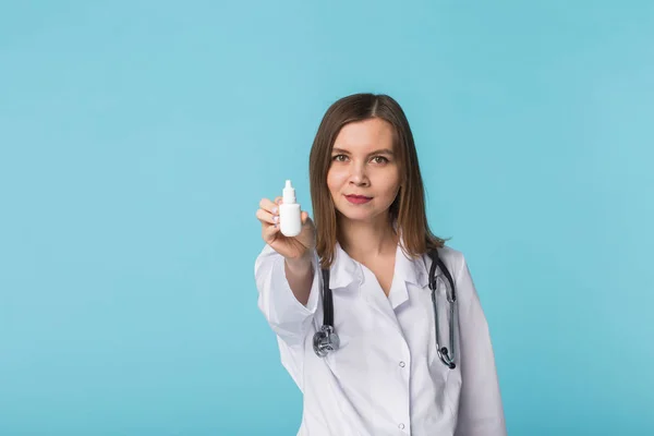 Medicaments and pharmaceutical concept - Young female doctor or pharmacist holding nasal spray on blue background