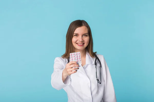Atrakcyjna lekarka Wyświetlono różowe pigułki. Piękny młody lekarz trzymając lekarstw na niebieskim tle. — Zdjęcie stockowe