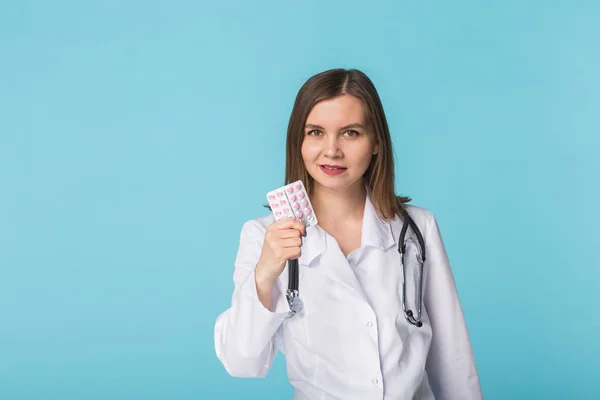 Ελκυστική γυναίκα γιατρό δείχνει ροζ χάπια. Όμορφη νεαρός γιατρός κρατώντας φάρμακα πάνω από μπλε φόντο. — Φωτογραφία Αρχείου