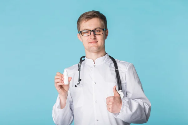 Ліки та фармацевтична концепція - чоловічий лікар або фармацевт, що тримає носовий спрей з великими пальцями на синьому фоні — стокове фото