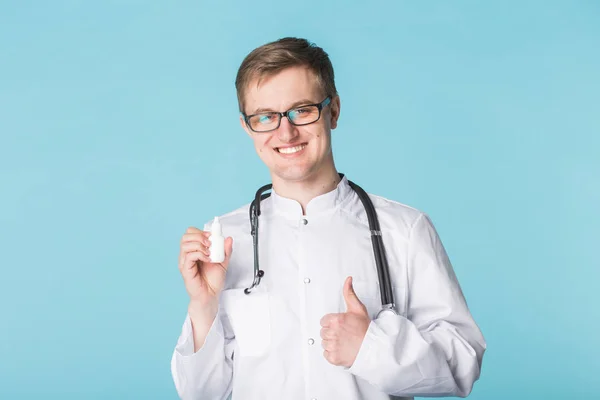 약 및 제약 개념-남성 의사 또는 약사 파란색 배경에 엄지손가락으로 비 강 스프레이 들고 — 스톡 사진