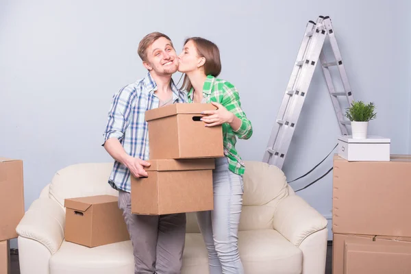 Moving, boxes and family concept - young couple having fun and kissing during relocation and holding the boxes — Stock Photo, Image