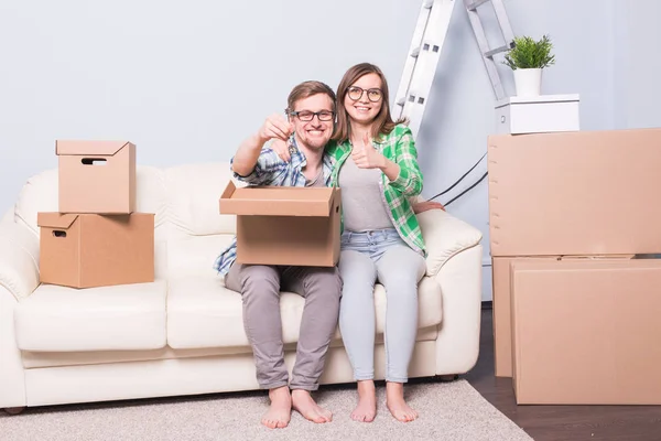 Переезд, переезд и новая концепция дома - молодая пара веселится на диване в окружении коробок — стоковое фото