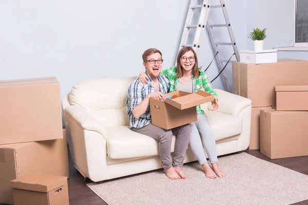 Семья, новая квартира, переезд и переезд - пара молодых счастливых людей вместе открывают коробку и чем-то удивляются — стоковое фото