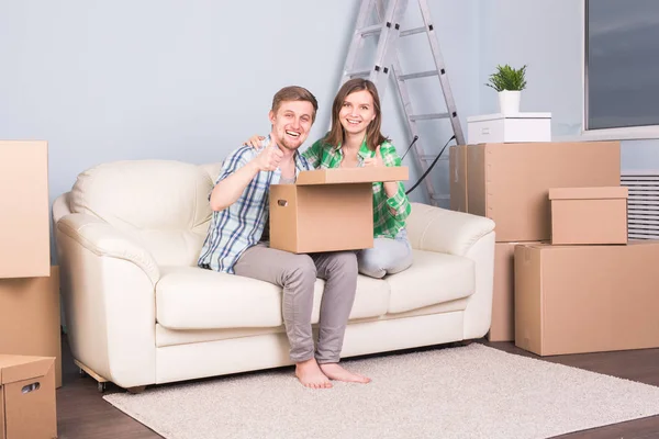 Relocation, new home and real estate concept - young couple sits on the couch and holding the box
