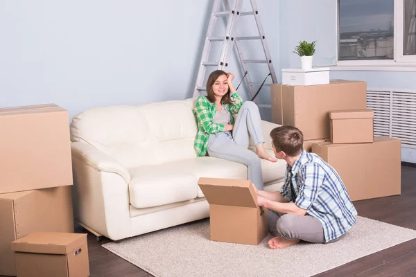 Moving, new apartment and relocation concept - young couple in the room surrounded by boxes having a small talk.