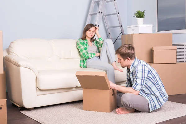 Moving, new apartment and relocation concept - young couple in the room surrounded by boxes having a small talk.