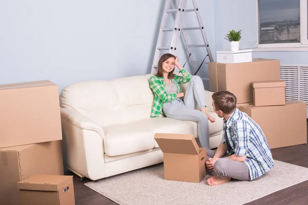 Umzug, neue Wohnung und Umzugskonzept - junges Paar im Zimmer, umgeben von Kisten mit Smalltalk. — Stockfoto