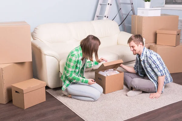 Концепция переезда и недвижимости - счастливая пара весело распаковывает картонные коробки в новом доме — стоковое фото