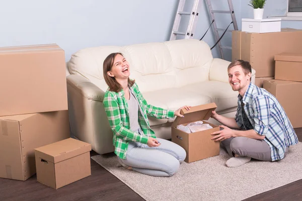 Концепция переезда и недвижимости - счастливая пара весело распаковывает картонные коробки в новом доме — стоковое фото