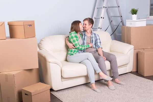 Концепция переезда и недвижимости - Счастливая пара целуется на диване в своей новой квартире — стоковое фото