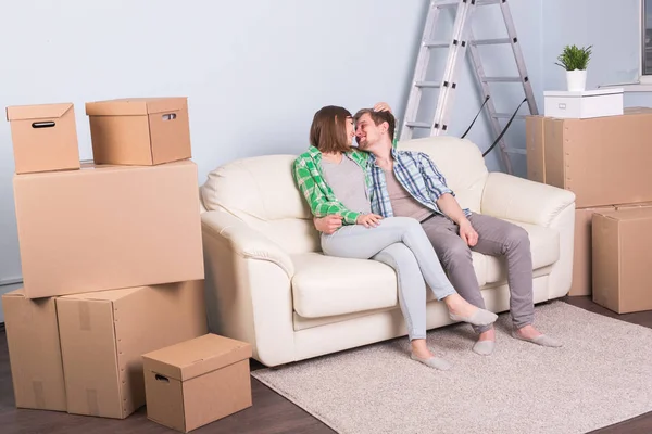 New home, relocation and moving concept - young couple sitting and kissing on the couch surrounded with boxes