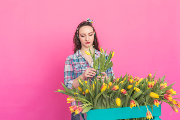 Happy caucasian young woman with box of yellow tulips on pink background