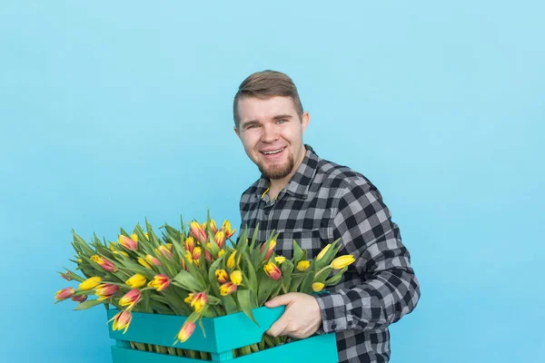 Jardineiro masculino caucasiano com caixa de tulipas rindo em fundo azul — Fotografia de Stock