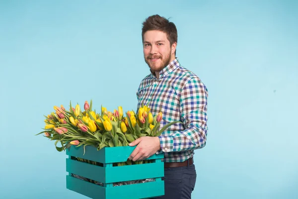 Bonito homem branco segurando uma caixa com tulipas amarelas no fundo azul — Fotografia de Stock