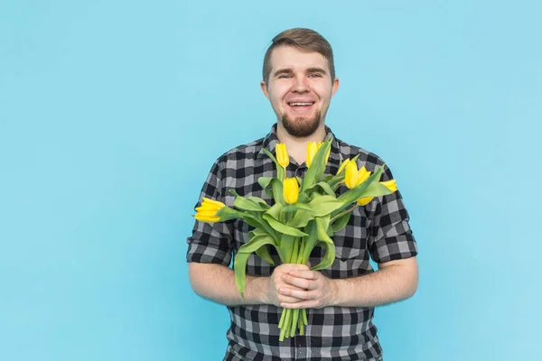 Homem bonito caucasiano com um monte de tulipas amarelas no fundo azul . — Fotografia de Stock