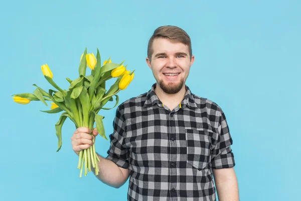 Handsome young man with bouquet of yellow tulips on blue background