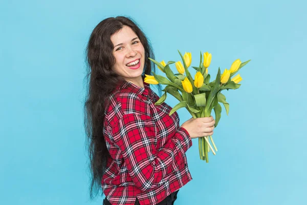 Směje se mladá Kavkazský žena s kyticí tulipánů na modrém pozadí. — Stock fotografie