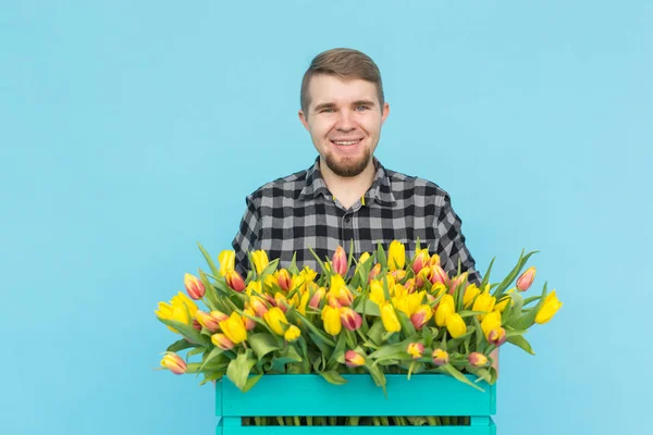 Alegre homem bonito florista segurando caixa de tulipas no fundo azul — Fotografia de Stock