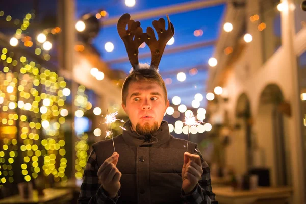 Personas, vacaciones y el concepto de Navidad - joven divertido en traje de venado de Navidad con bengala luz al aire libre — Foto de Stock